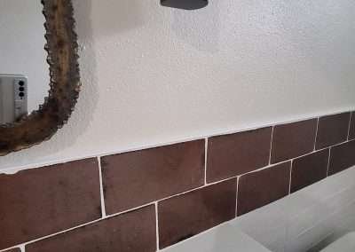 Close-up of a brown tile backsplash, and part of a decorative mirror frame in a bathroom.