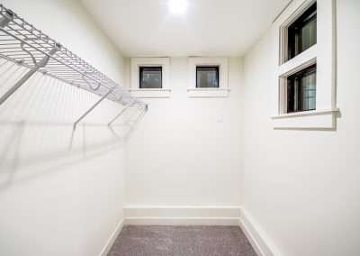 A bright walk-in closet with wire shelving and small windows, featuring ample storage space.