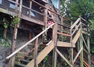A wooden staircase leading up to a house exterior with damaged lattice.