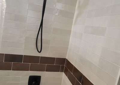 A modern shower featuring a black matte rainfall showerhead, beige wall tiles, and a small glass block window.