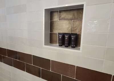 A shower wall featuring built-in storage niches with decorative brown tiles, surrounded by glossy beige tiles and a horizontal accent strip.