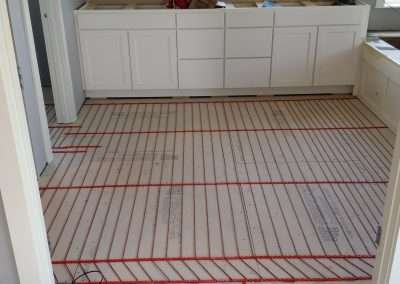 A bathroom under renovation, showing the installation of an underfloor heating system with red heating cables laid out across the floor.
