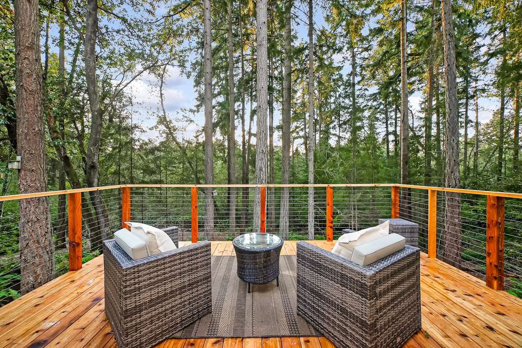 Spacious outdoor deck with comfortable wicker furniture, surrounded by lush trees.