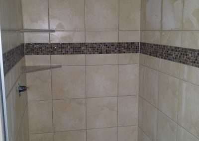 Shower enclosure with beige tiles and a brown mosaic tile border.