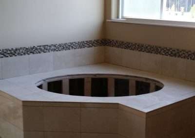 Bathroom renovation featuring a circular bathtub platform surrounded by beige tiles and a decorative mosaic tile border.