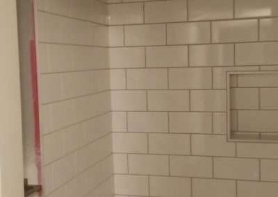 A close-up of a shower surround with white subway tiles and a built-in shelf.