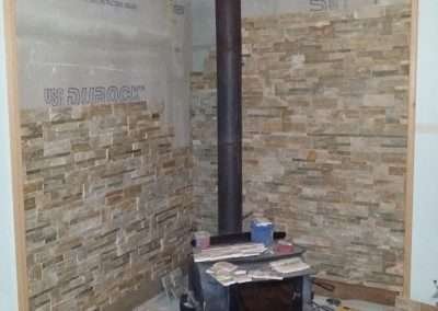 A corner fireplace under construction with a wood stove and Durock cement board.