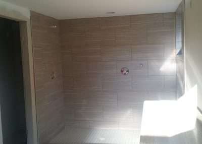 Shower enclosure with large gray tiles and a white tiled floor. Construction in progress.