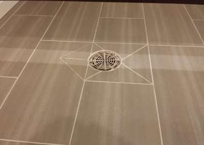 Close-up of a grey tiled floor with a circular drain in the center.