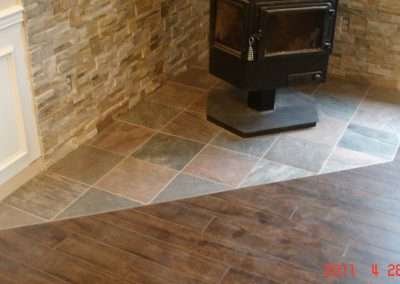 Rustic fireplace with a stone surround, tiled hearth, and dark wood flooring.
