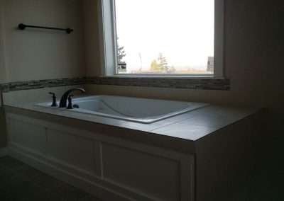 White freestandi ng bathtub with black faucets, a decorative tile border, and a towel rack. Large window with a view.
