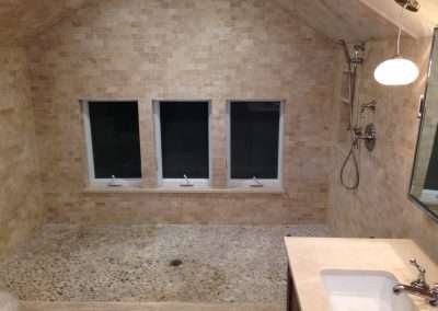 A luxurious bathroom with a spacious shower featuring a pebble floor, multiple showerheads, and large windows.
