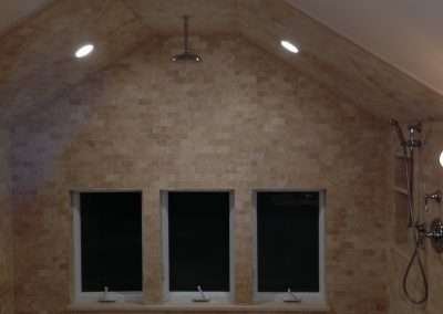 A rustic bathroom with a large shower featuring a pebble floor, stone tile walls, and a single window.