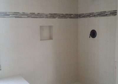 A modern shower with white subway tile walls and a decorative tile border.