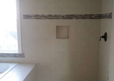 A modern walk-in shower with white subway tile walls, a decorative tile border, and a recessed shelf.
