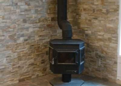 A black wood stove in a corner fireplace surrounded by a stone wall.