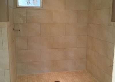 A spacious walk-in shower with beige tiles and a small window.