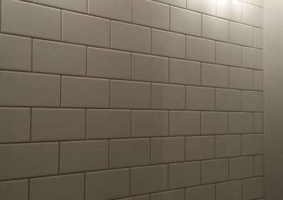 A white tile backsplash with white grout, illuminated by overhead lights.