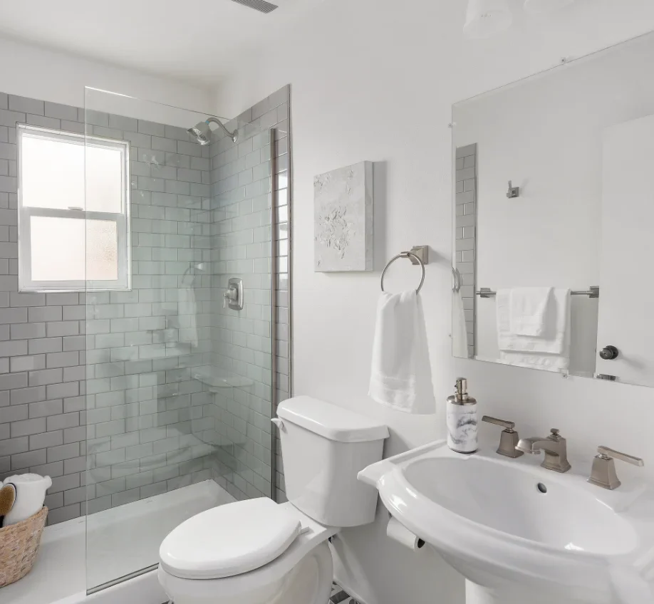 A stylish bathroom with patterned floor tiles, a glass shower, white fixtures, and grey subway tiles