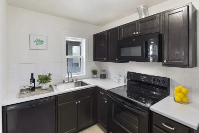A modern kitchen featuring a large island with white cabinets and a light countertop, and a black cutting board on the island.