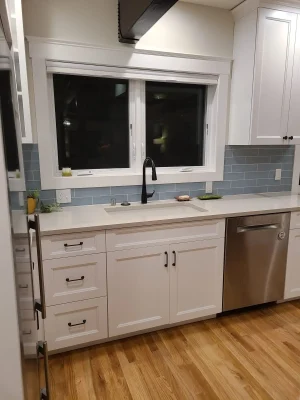 Modern kitchen with white cabinetry, black faucet, blue subway tile backsplash, and stainless steel dishwasher in a Seattle home remodel.