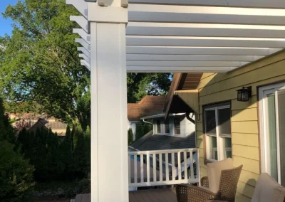 Partially completed small deck with black metal railing attached to a beige house, showing unfinished construction details and structural supports.