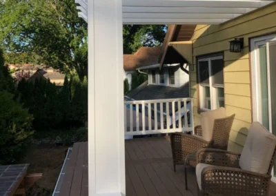 Partially completed small deck with black metal railing attached to a beige house, showing unfinished construction details and structural supports.