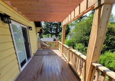 Spacious composite deck with a custom wooden pergola and decorative railing, attached to a yellow Bellevue home. Expertly built by deck and patio contractors in Bellevue for enhanced outdoor living and relaxation.