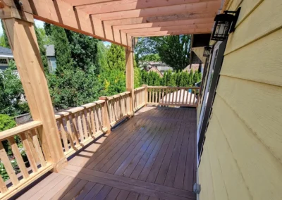 Spacious composite deck with a custom wooden pergola and decorative railing, attached to a yellow Bellevue home. Expertly built by deck and patio contractors in Bellevue for enhanced outdoor living.