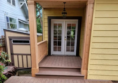 Custom-built composite deck with a wooden pergola and covered entryway, leading to French doors of a Bellevue home. Designed by expert deck and patio contractors in Bellevue for elegance and durability.