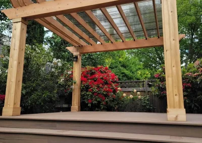 Custom-built wooden pergola with a transparent polycarbonate roof, set on a raised composite deck with wide steps in a landscaped Seattle backyard. Designed by expert patio and deck contractors in Seattle for beauty and functionality.