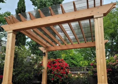 Custom-built wooden pergola with a transparent polycarbonate roof, set on a raised composite deck with wide steps in a landscaped Bellevue backyard. Designed by expert patio and deck contractors in Bellevue for beauty and functionality.