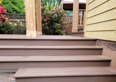 Custom composite deck stairs leading to a covered patio with a wooden pergola, surrounded by lush landscaping in a Bellevue backyard. Built by expert deck and patio contractors in Seattle for durability and aesthetic appeal.