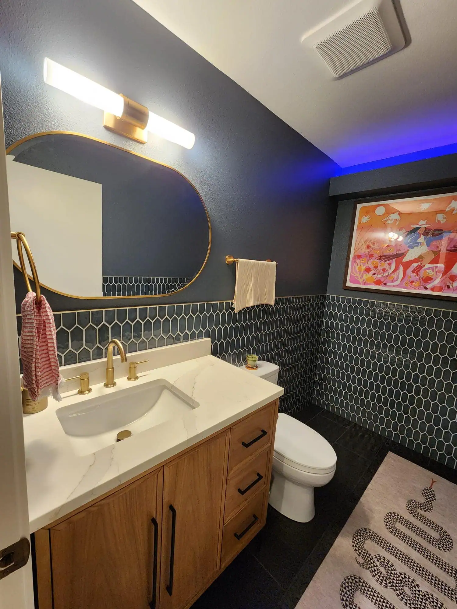 Seattle bathroom remodel featuring a modern wood vanity with a quartz countertop, gold fixtures, hexagonal tile backsplash, and ambient LED lighting.