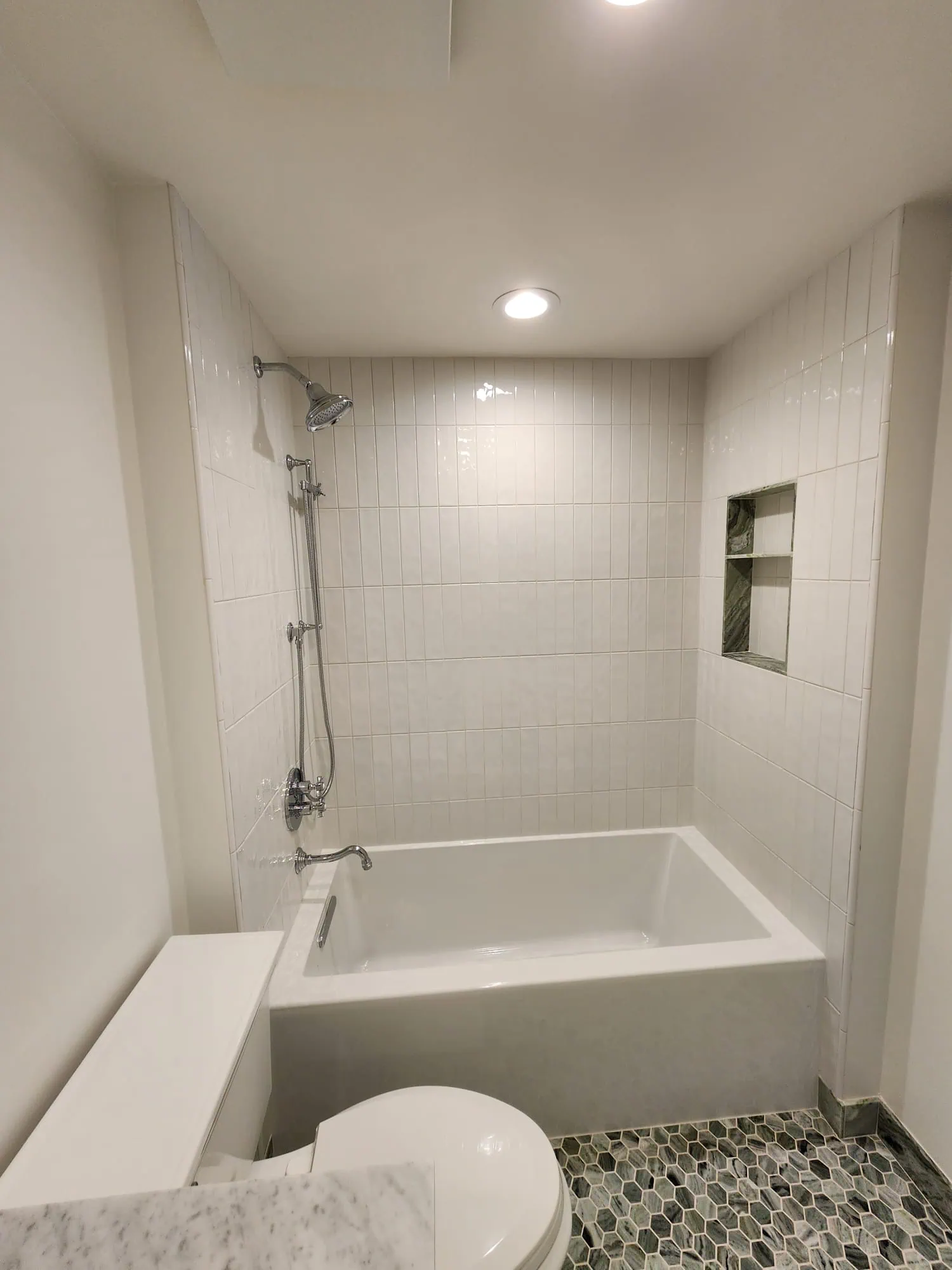Modern bathroom remodel in Seattle featuring a white bathtub, subway tile walls, a built-in niche, and hexagonal floor tiles.