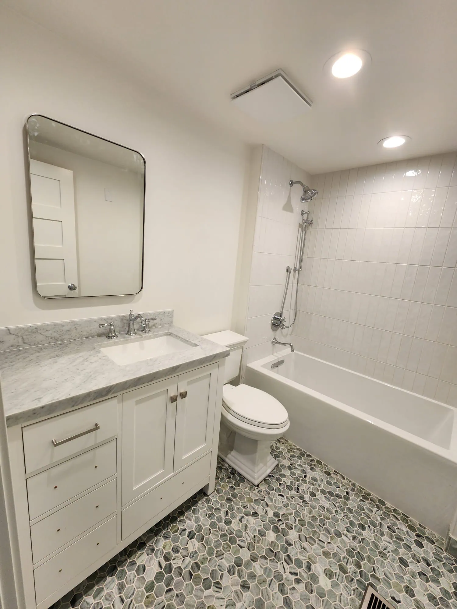 Seattle bathroom remodel with a white vanity, marble countertop, subway tile shower, and hexagonal stone flooring.