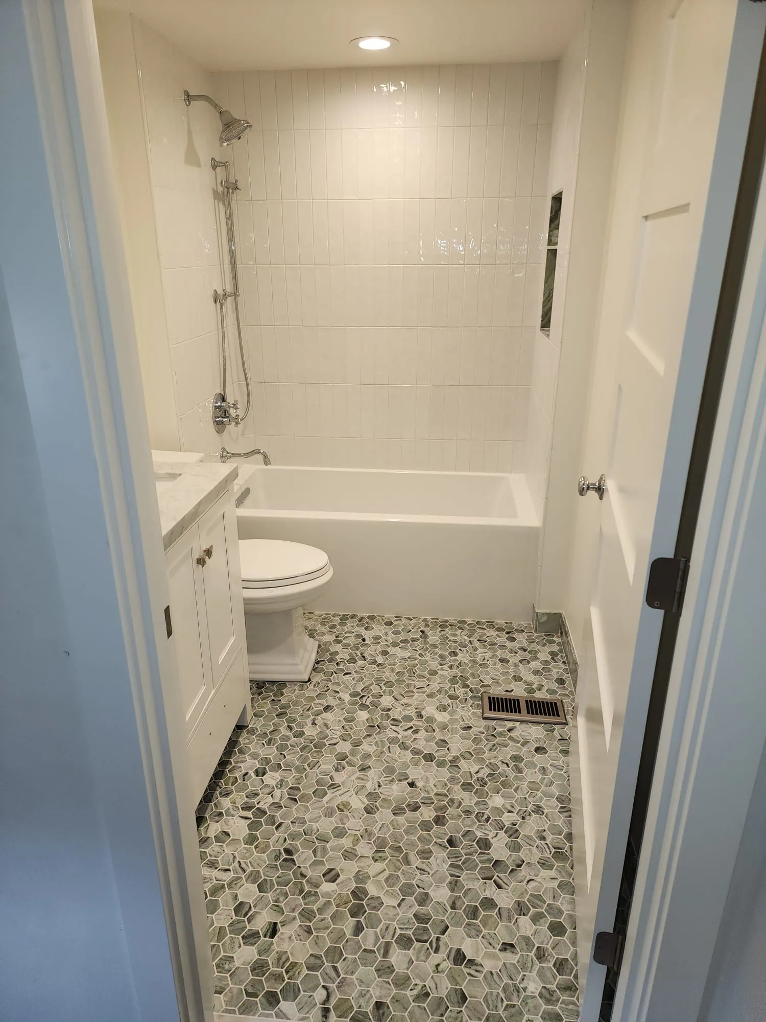 Completed Seattle bathroom remodel featuring a white bathtub, subway tile shower, built-in niche, and hexagonal stone flooring.