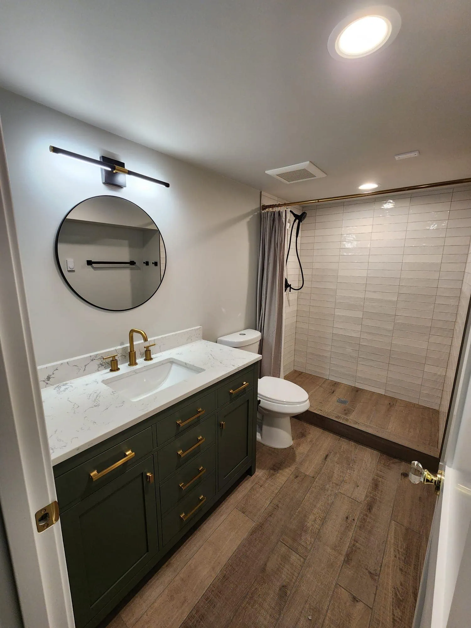 Seattle bathroom remodel featuring a green vanity with gold hardware, quartz countertop, walk-in shower, and wood-look flooring.