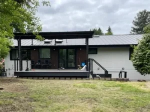 Bellevue 1 Spacious modern patio with a covered pergola, black metal railing, and composite decking, extending from a contemporary home in Seattle. Built by expert patio and deck contractors in Seattle for comfort and style.