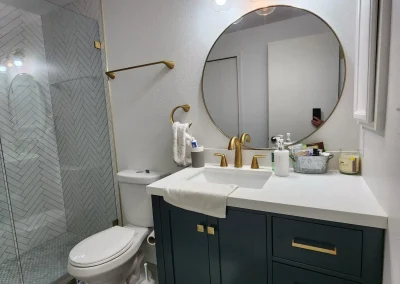 Seattle bathroom remodel featuring a navy vanity with gold hardware, a round mirror, modern lighting, and a herringbone tile shower.