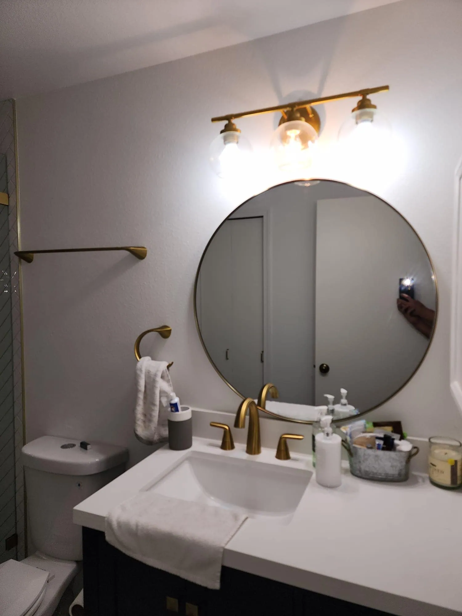 Seattle bathroom remodel featuring a modern vanity with a white quartz countertop, gold fixtures, a round mirror, and elegant lighting.