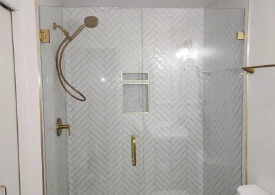 Seattle bathroom remodel featuring a glass-enclosed herringbone tile shower with gold fixtures and a built-in niche.