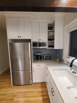 Modern kitchen with white cabinetry, stainless steel refrigerator, built-in microwave, and blue subway tile backsplash in a Seattle home remodel