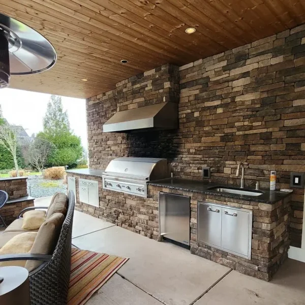 High-end home addition in Seattle featuring a covered outdoor bar and lounge area with a wood-paneled ceiling, built-in lighting, and stone countertops, designed by expert home addition contractors in Seattle.