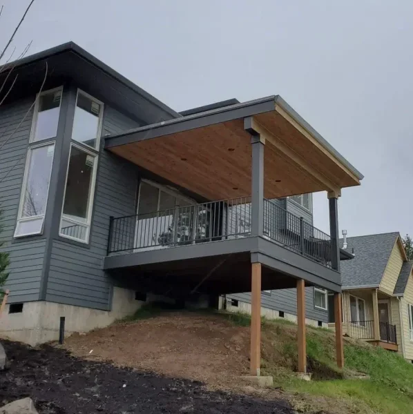 Modern elevated deck with a covered roof and black metal railing, supported by wooden posts on a sloped yard in Seattle. Built by expert deck contractors in Seattle for stability and style.