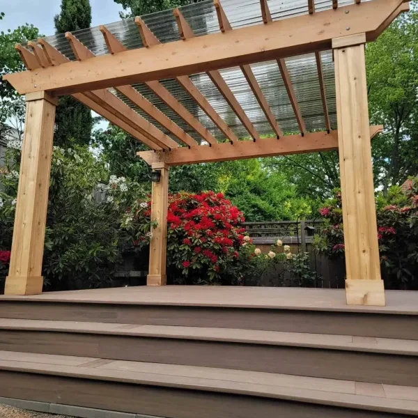 Custom-built wooden pergola with a transparent polycarbonate roof, set on a raised composite deck with wide steps in a landscaped Seattle backyard. Designed by expert patio and deck contractors in Seattle for beauty and functionality.