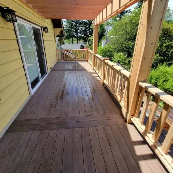 Spacious composite deck with a custom wooden pergola and decorative railing, attached to a yellow Seattle home. Expertly built by deck and patio contractors in Seattle for enhanced outdoor living and relaxation.