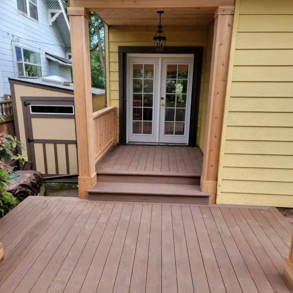 Custom-built composite deck with a wooden pergola and covered entryway, leading to French doors of a Seattle home. Designed by expert deck and patio contractors in Seattle for elegance and durability.