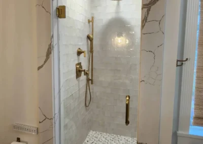 A walk-in shower framed by a thick-veined marble slab portal featuring brushed gold hardware and Zellige-style wall tiles.