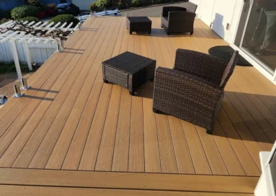 Luxury composite deck with wicker lounge furniture and frameless glass railings overlooking a territorial view.